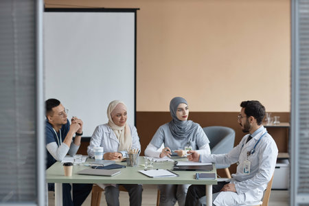 Medium full shot of Muslim medical interns listening to experienced male supervisors instructions during meeting in clinic officeの写真素材