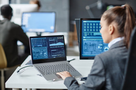 Over shoulder view of female IT security specialist using multiple computers with blue data on...