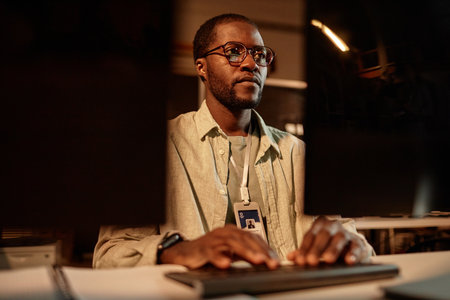 Portrait of Black computer programmer wearing glasses working in office at night