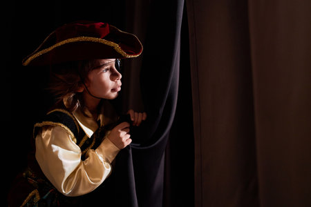 Side view portrait of little boy wearing costume peeking over curtain backstage in theater copy spaceの写真素材
