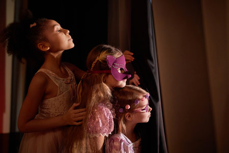 Side view portrait of three little girls wearing costumes peeking over curtain backstage in theater copy spaceの写真素材