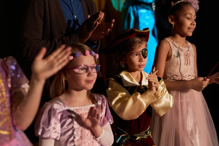 Portrait of cute little boy wearing pirate costume standing on stage in theater and applauding with...