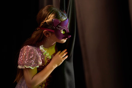 Side view portrait of young girl wearing costume peeking over curtain backstage in theater copy spaceの写真素材
