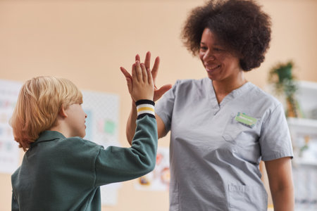Waist up portrait of African American friendly nurse high five with little boy in doctors office