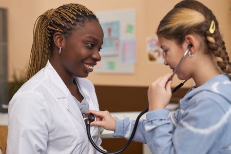 Side view portrait of young girl enjoying medical examination in clinic and playing with stethoscope listening to doctors heartの写真素材