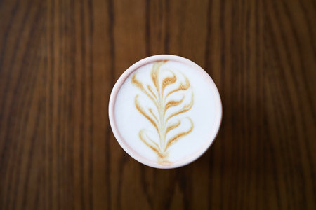 Minimal top view of coffee cup with latte art swirls in foam on wooden table