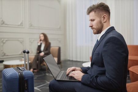 Side view portrait of successful young businessman using laptop in hotel lobby during work trip, copy spaceの写真素材