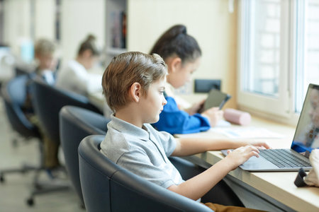 Side view portrait of young boy using laptop computer in school during IT class for childrenwith copy spaceの写真素材
