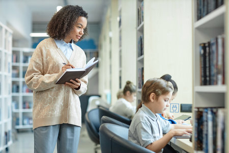 Side view portrait of Black young woman as teacher watching children working with computers during...