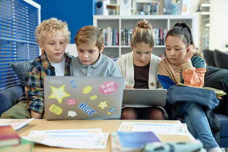 Front view at group of young teenagers using computers together during break in school libraryの写真素材