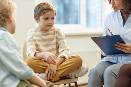 Full length portrait of sad young boy sitting with legs crossed on chair in support group circle for children and teenagerswith copy spaceの写真素材