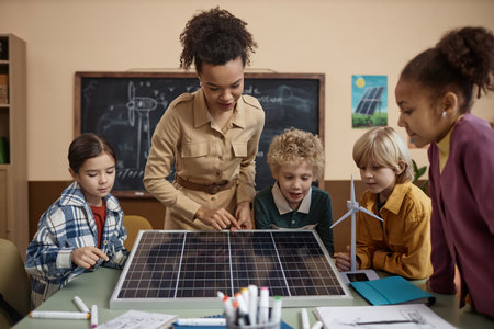 Diverse group of children learning about renewable energy in school with young teacher sowing solar panel to classの写真素材
