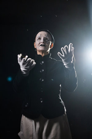 Minimal portrait of emotional mime artist playing drama on stage against black background and...
