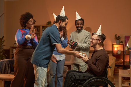 Side view portrait of adult man with disability celebrating Birthday party with friends presenting...