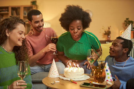Portrait of adult Black woman blowing candles on Birthday cake and enjoying party celebration with friends at homeの写真素材