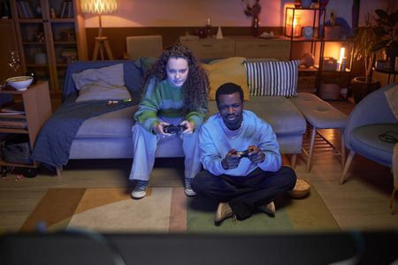 Full length portrait of two friends man and woman playing videogame in living room sitting on couch in dark homeの写真素材