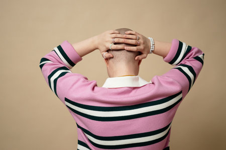 Minimal back view of bald young woman with hands on head, alopecia and cancer survivor conceptの写真素材