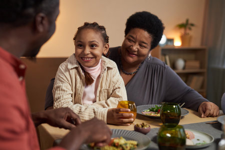 Portrait of smiling Black grandmother at dinner table with little girl and family enjoying conversationの写真素材