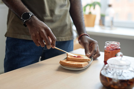 Close up of unrecognizable African American man making peanut butter and jelly sandwich at kitchen table for breakfast copy spaceの写真素材