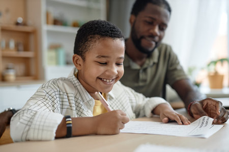 Portrait of smiling Black boy doing homework at kitchen table with father helping copy spaceの写真素材