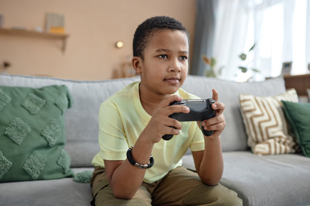 Portrait of young African American boy playing video game at home and holding controller with...