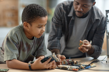 Portrait of young Black boy repairing computer parts with father at home, copy space