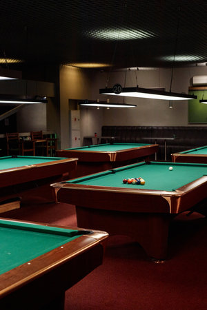 Vertical background image of low lit pool club with several billiard tables and no people copy space