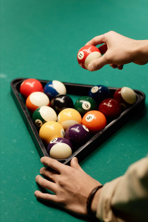 Minimal closeup of unrecognizable man holding red billiard ball while playing pool at green table...