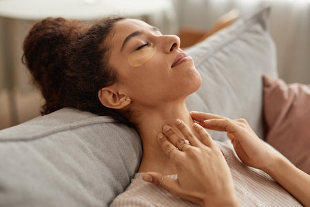 Side view portrait of blissful young woman enjoying self care day at home and doing face and neck...