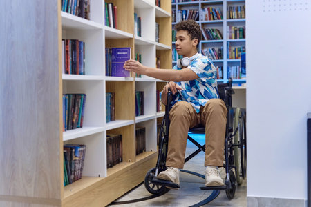 Full length portrait of Middle Eastern teenage boy with disability choosing books in school library, copy spaceの写真素材