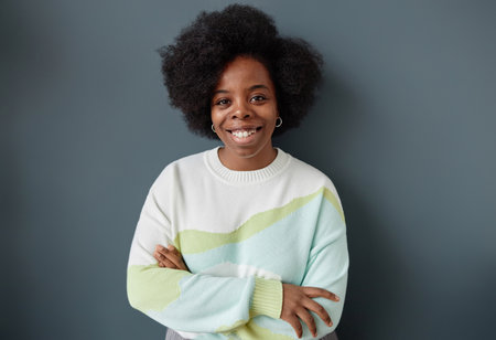 Minimal waist up portrait of smiling Black woman with natural hair standing against grey wall dressed in casual clothes and looking at camera studio shotの写真素材