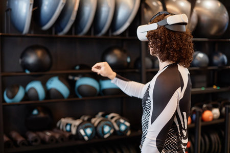 Back view of sportive young man using VR technology for immersive training experience in gym copy...