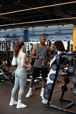 Vertical full length portrait of muscular African American man as fitness coach greeting clients in...