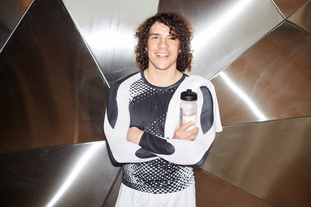 Waist up portrait of young muscular man smiling at camera posing wearing reflective sportswear, shot...