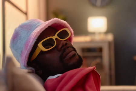 Close up portrait of Black young man wearing fuzzy bucket hat and sunglasses looking at camera...