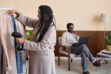 Side view portrait of African American woman steaming delicate garment on hanger in fashion studio, copy spaceの写真素材