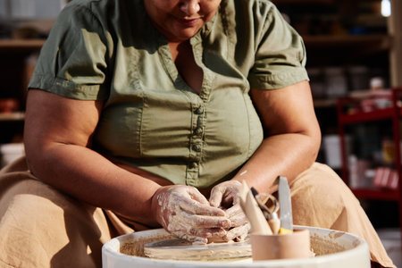 Cropped shot of African American senior woman creating handmade ceramics at pottery wheel in art studio lit by sunlight copy spaceの写真素材