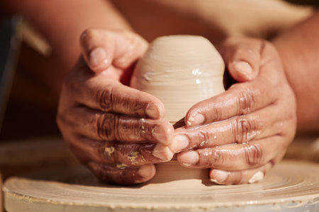 Front view closeup of gentle female hands shaping clay on pottery wheel enjoying crafting process in sunlightの写真素材
