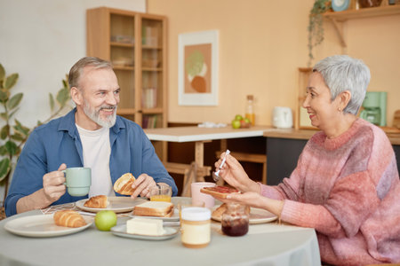 Portrait of happy senior couple enjoying breakfast together in cozy kitchen and smiling looking at...
