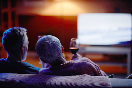Back view of senior couple watching movie together sitting on couch at home copy spaceの写真素材