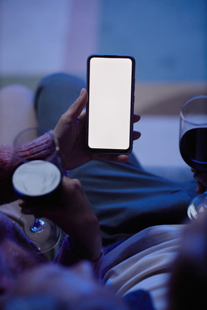 Vertical closeup of hand holding phone with blank white screen and using mobile app in blue lightの写真素材