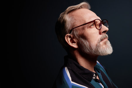 Side view portrait of bearded senior man wearing glasses on dark background, copy space
