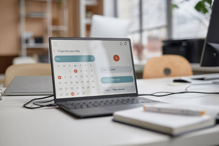 Close up shot of laptop at workplace table. Computer screen displaying calendar with month of May, focus on screen, copy spaceの写真素材