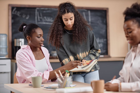 Multicultural team of three working together at desk in modern office space. Multiethnic students collaborating preparing for exam discussing notes in notepad in school setup, copy spaceの写真素材