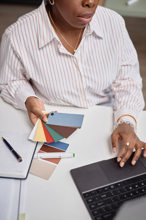 Vertical close up shot of Black business woman female holding multicolored paper swatches against working desk with laptop and pens, creativity work concept, copy spaceの写真素材