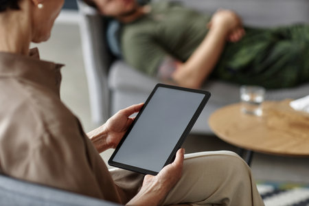 Over shoulder closeup of female psychologist holding digital tablet with blank while screen while consulting client in therapy session copy spaceの写真素材