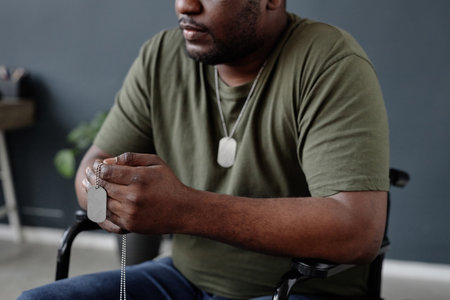 Close up of Black adult man as army veteran with disability using wheelchair and holding dog tags necklace copy spaceの写真素材