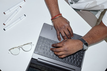Top view closeup of unrecognizable Black man using laptop with modern business accessories and watch...