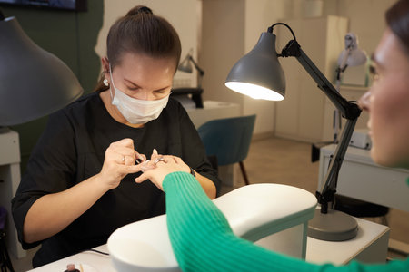 Shot of young female customer getting nails done and manicurist at work wearing face mask in beauty studio, copy spaceの写真素材