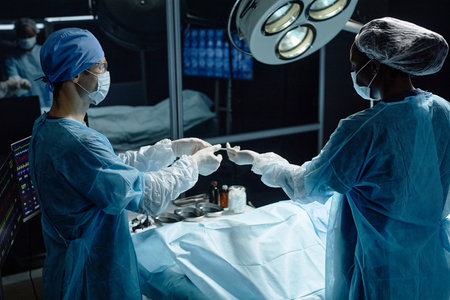 Side view portrait of medical assistant handing tools to surgeon performing surgery in operating roomの写真素材